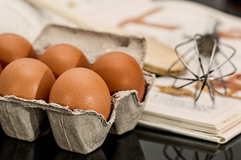 Eggs in a carton on a desk next to a cookbook.