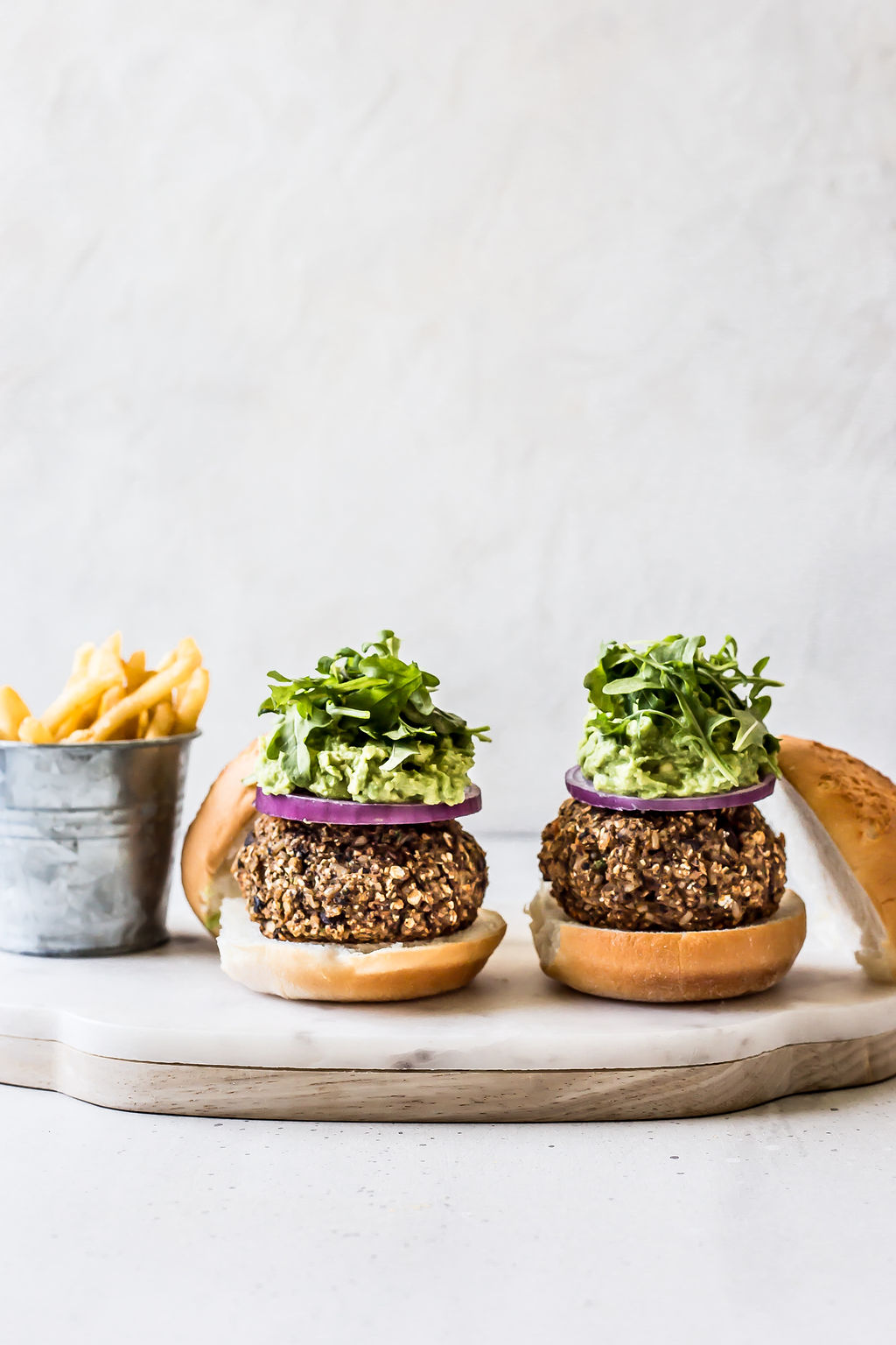 Two burgers on a wooden plate and jar of french fries.