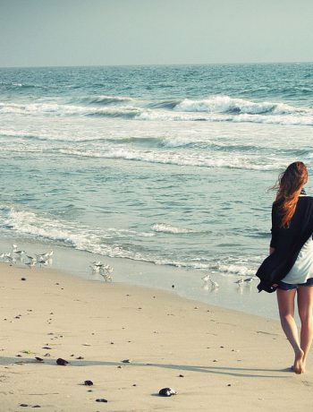 Woman walking on the beach alongside the ocean.