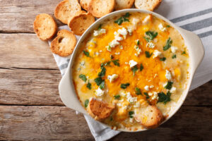 buffalo chicken dip in a white dish with toasted bread on a table and white and gray napkin
