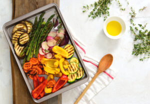 roasted vegetables on a baking tray with butter and thyme on a wooden and white background