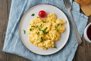Scrambled eggs on a white plate and light blue napkin