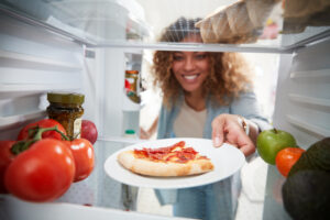 woman taking out leftover pizza from fridge 