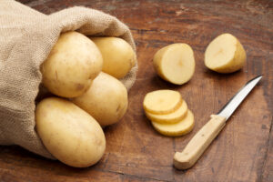 Raw potatoes on a table being cut with a knife