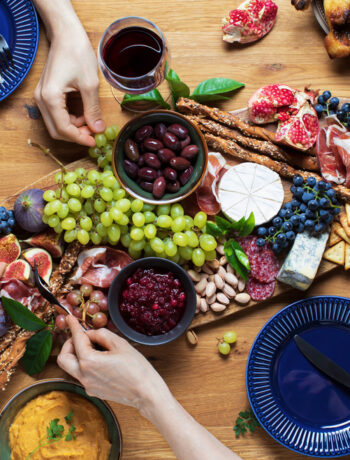 People eating a charcuterie board with fruit, meat, cheese, and crackers with a wooden background