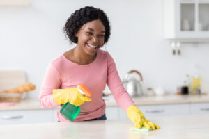 Woman cleaning a kitchen counter using spray and a sponge wearing cleaning gloves
