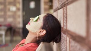 A beautiful woman with facial clay mask on face and fresh cucumber on eyes relaxing at Home. Portrait of beautiful spa girl. Beauty, healthcare.