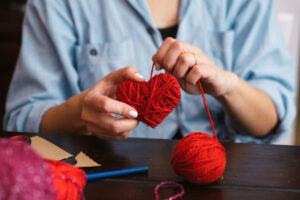 Woman wrapping yarn around cardboard heart to create a heart 