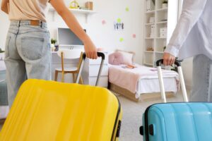 Female students with suitcases in dorm room on moving day, back view