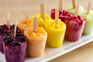 Assorted flavors of homemade fresh pureed frozen fruit popsicles sitting on white plate in a row 