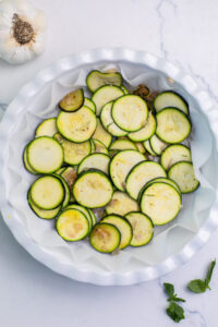 adding a layer of zucchini into the pie plate.