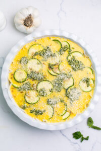adding another layer of egg, zucchini, and pesto to the pie plate.